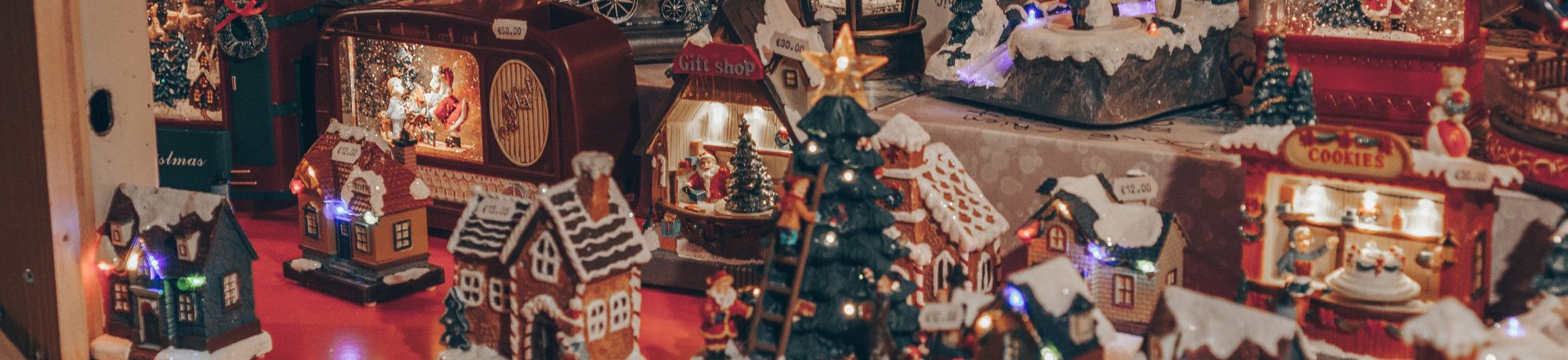 Festive miniature Christmas village with snow-covered houses and twinkling lights on a red table surface