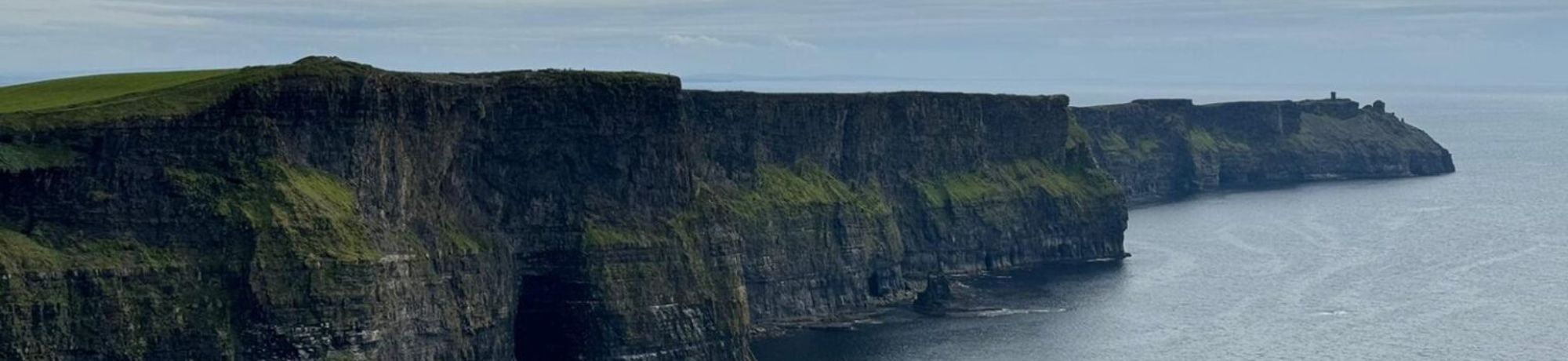 Steep sea cliffs along a rocky coastline with green grass on top and the ocean to the right.