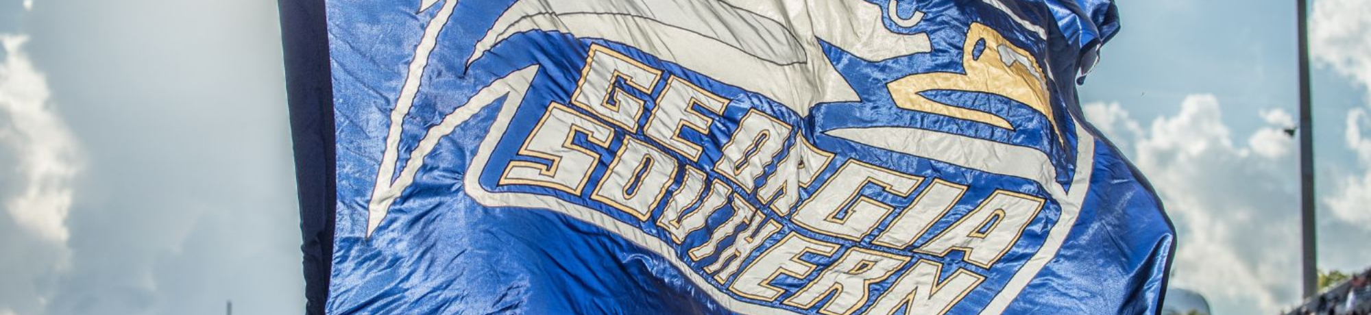 Georgia Southern University flag waving in the wind outdoors, blue and white colors with the words Georgia Southern visible beneath the sunlit sky.